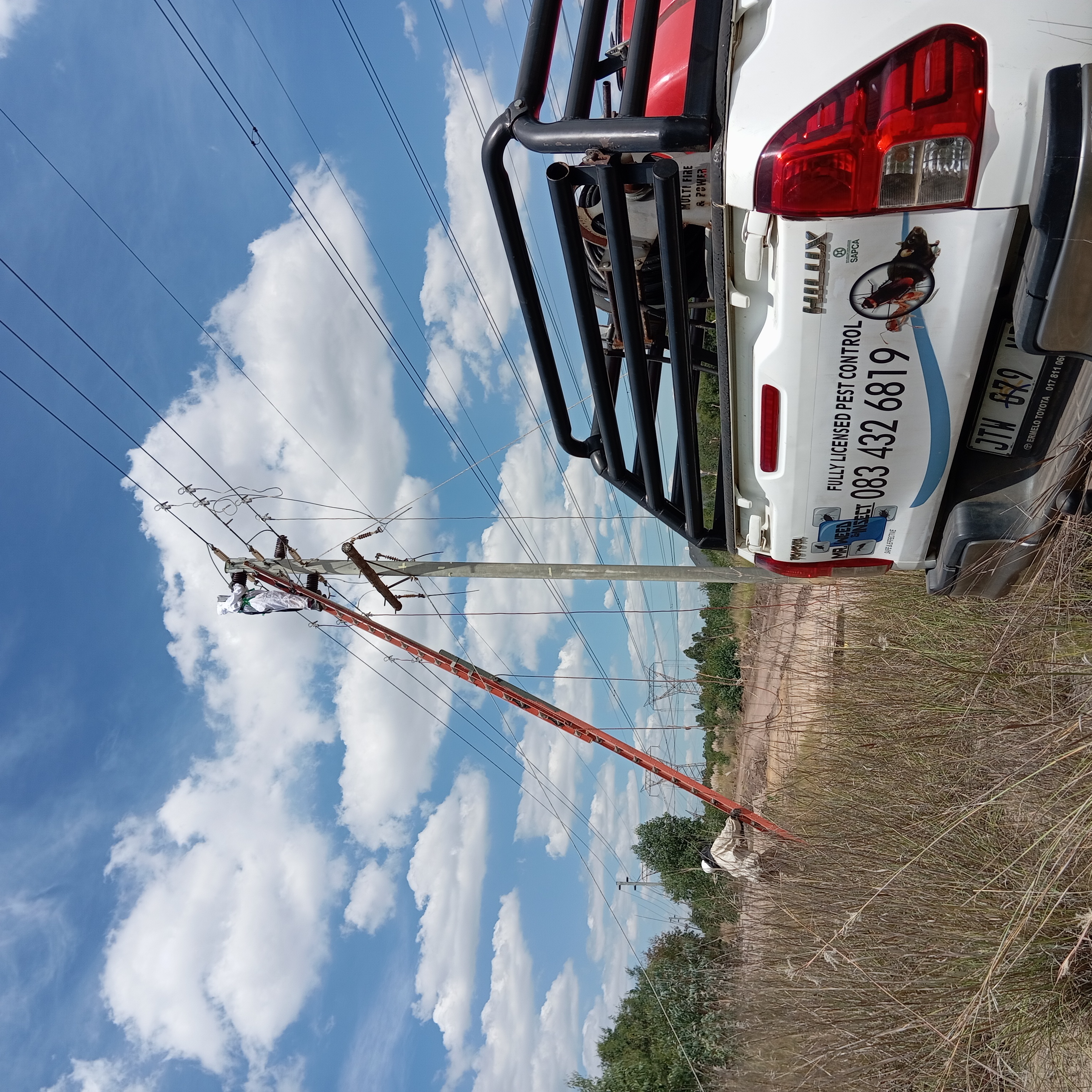 Technician in protective gear climbs a tall ladder leaning against a utility pole to work on power lines.
