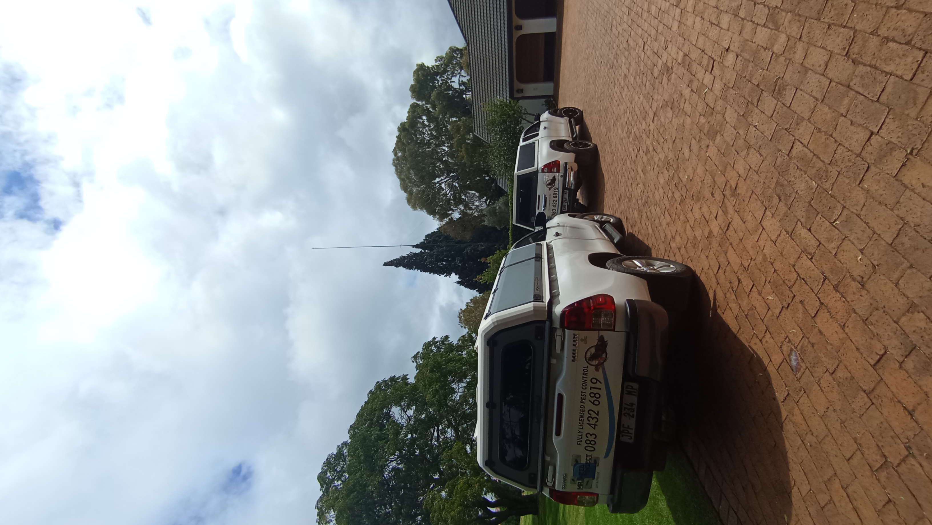 Two white pickup trucks with pest control decals parked on a red brick driveway under a cloudy sky.
