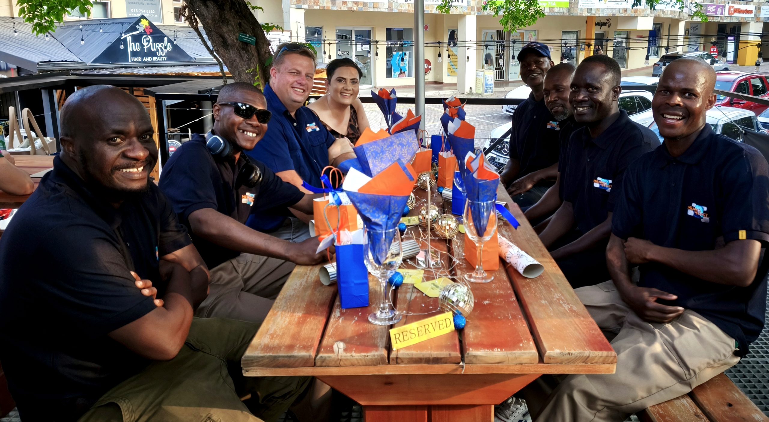 Group of colleagues smiling while sitting at a reserved wooden table decorated with blue and orange paper cones.